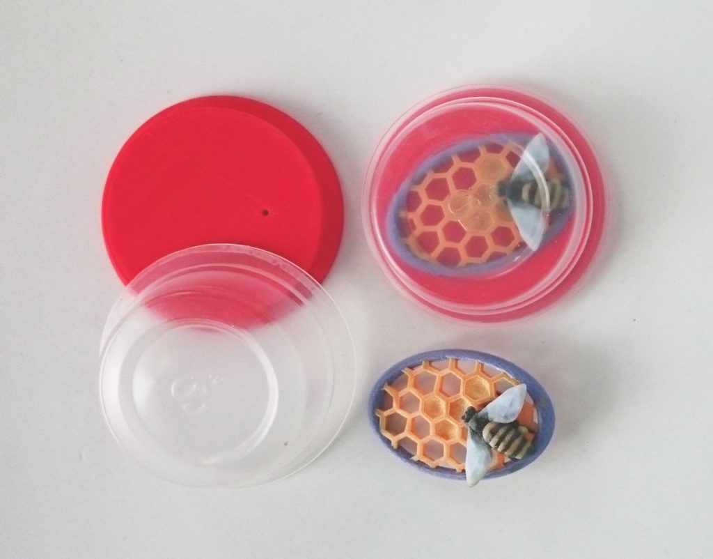 Plastics are precious: Ann Marie Shillito's 'Bee Brooch'. Ann Marie designed the red 3D printed lid to fit a clear plastic tub from Simply Cook which she has repurposed here as a packaging and display box.