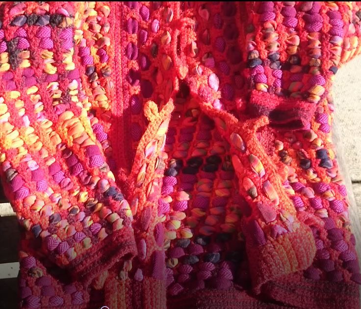 Sustainable Me: Image shows a jacket made by Ann Marie Shillito, crocheted in waste carpet wool, woven with strips of waste fabric in reds, oranges, pinks and purples. 